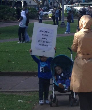 Child holding sign demanding people be beheaded